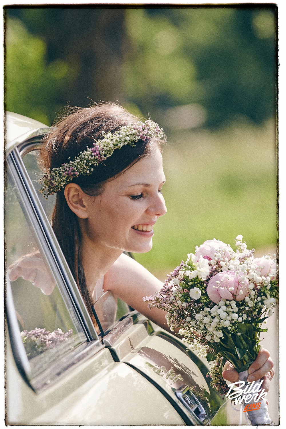 Foto: Copyright - Paul Walther - Ein Brautportrait in einem alten Alpha Romeo. Sie lehnt sich aus dem Fenster, hat einen Brautstrauß mit rosa und weißen Blumen in der Hand und trägt einen Blumenkranz im Haar.